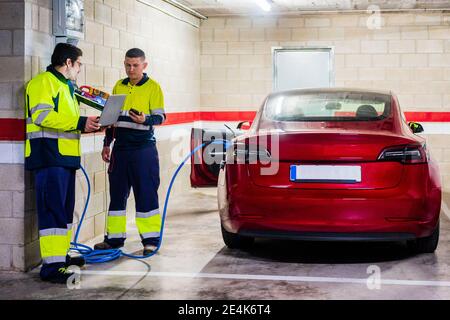 Male programmers discussing over laptop while charging electric car Stock Photo