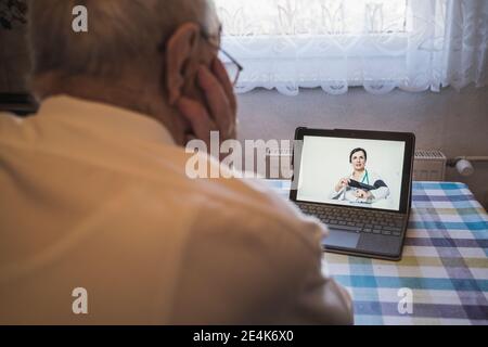 Female doctor showing male patient how to check blood pressure on video call through laptop at home Stock Photo