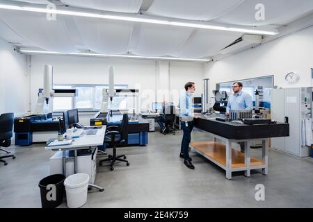 Engineers talking while standing in measuring room at office Stock Photo