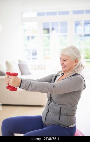 Smiling retired senior woman exercising with dumbbells at home