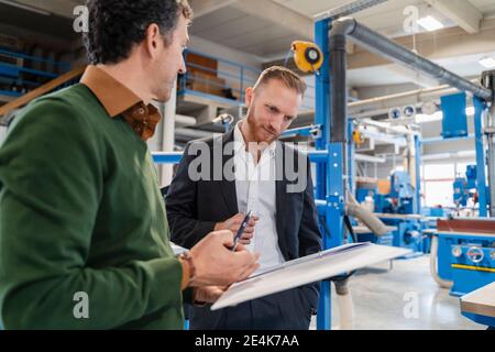 Two carpenters talking over documents in production hall Stock Photo