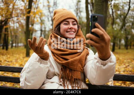 Smiling young woman hand gesturing while talking on video call in autumn park