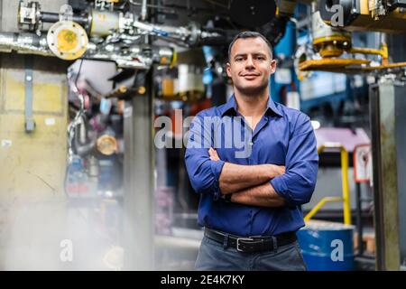 Smiling mature supervisor with arms crossed in industry Stock Photo