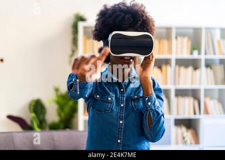 Woman wearing virtual reality headset stretching hand while standing at home Stock Photo