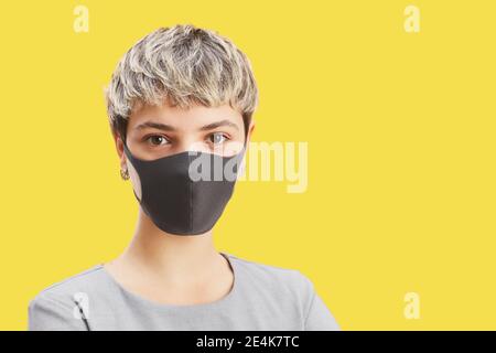 Head and shoulders portrait of contemporary short-haired woman wearing mask while standing against pop yellow background, copy space Stock Photo