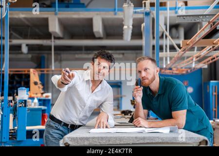 Two carpenters talking over documents in production hall Stock Photo