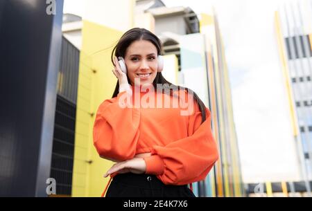 Portrait of beautiful brunette standing outdoors and smiling while listening to music on headphones Stock Photo