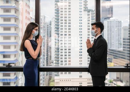 Young caucasian business colleague wearing face mask with thai style greeting for social distanting concept in new normal office at downtown