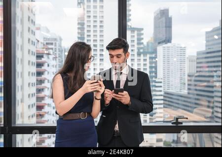 Young caucasian business colleague using smartphone and discussing in modern office at business district Stock Photo