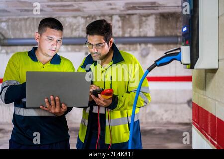 Professional male programmers discussing while working on laptop in auto repair shop Stock Photo