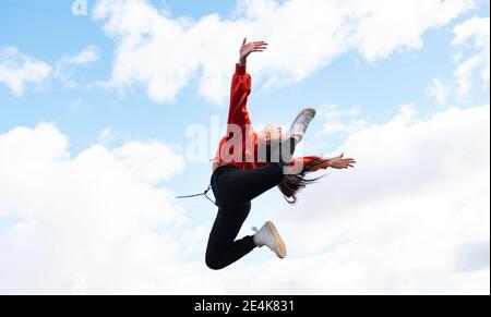 Long-haired brunette jumping against sky Stock Photo