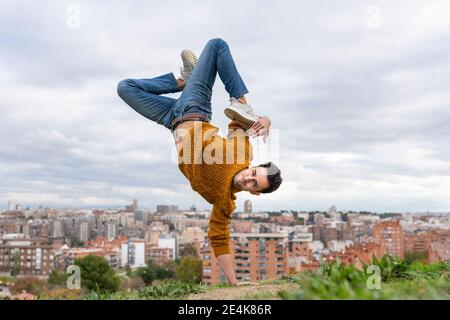 Flexible young man doing handstand on hill in city against sky Stock Photo