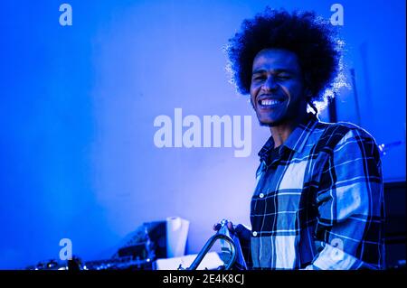 Afro young man playing trumpet against wall in blue living room Stock Photo