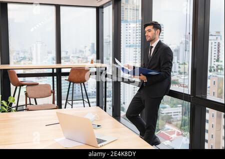 Young caucasian businessman holding financial document and looking in modern office at business district Stock Photo