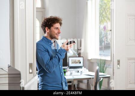 Male professional sending voicemail through mobile phone at office Stock Photo