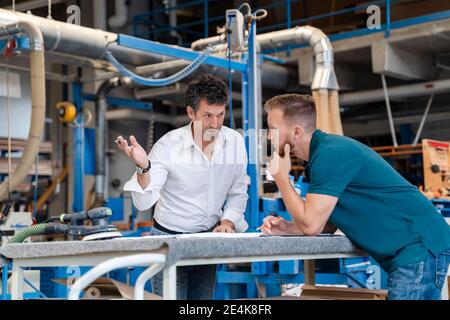 Two carpenters talking over documents in production hall Stock Photo