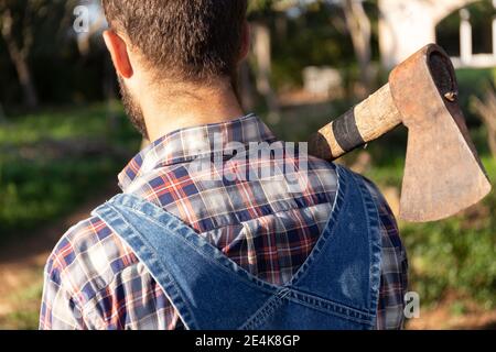 Man in coveralls carrying axe on sunny day Stock Photo
