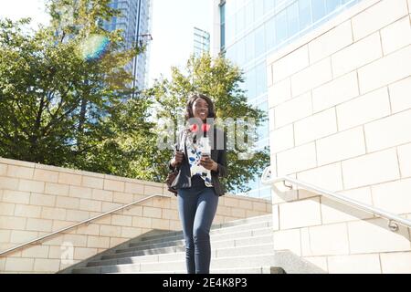 Businesswoman with headphones and mobile phone carrying backpack while walking on staircase Stock Photo