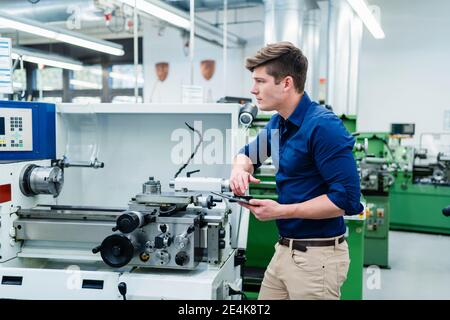 Male engineer looking away with digital tablet while standing by machinery in factory Stock Photo