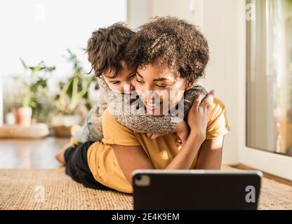 Smiling mother with son using digital tablet while lying at home Stock Photo