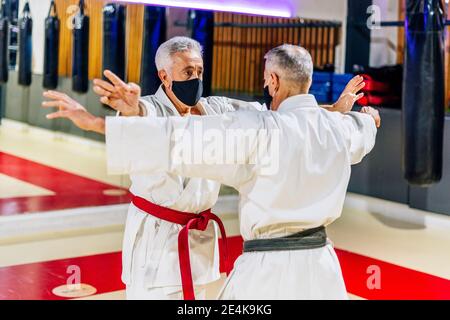 Men with arms outstretched wearing face masks while practicing karate in health club Stock Photo