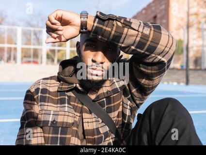 Young man with blank expression shielding eyes in sports court on sunny day Stock Photo