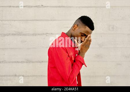 Young man in red jacket against concrete wall Stock Photo