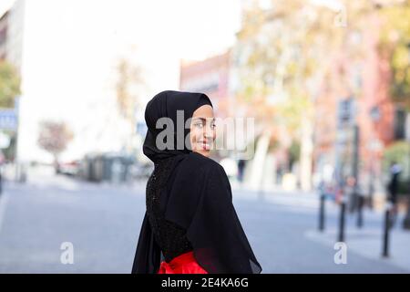 Portrait of young beautiful woman wearing black hijab looking over shoulder and smiling at camera Stock Photo
