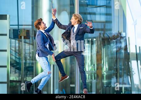 Excited business people giving high five while jumping against glass Stock Photo