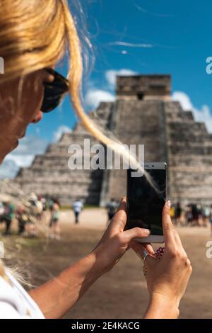 Mexico, Yucatan, Chichen Itza, Hands of female tourist taking smart phone photos of Temple Of Kukulcan Stock Photo