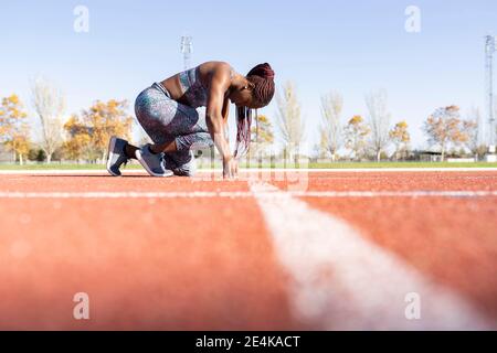 Female athlete in ready position on running track during sunny day Stock Photo