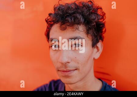 Close-up portrait of handsome man with curly hair against orange wall Stock Photo