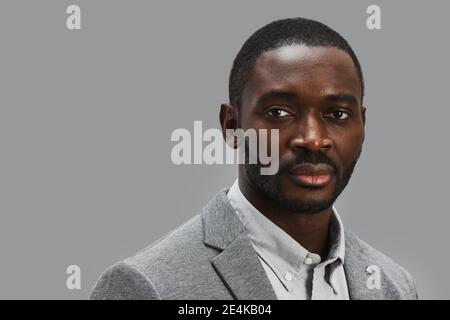 Minimal head and shoulders portrait of confident African-American businessman looking at camera while standing against gray background, copy space Stock Photo