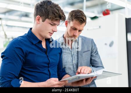 Male colleagues discussing over file document while standing in factory Stock Photo