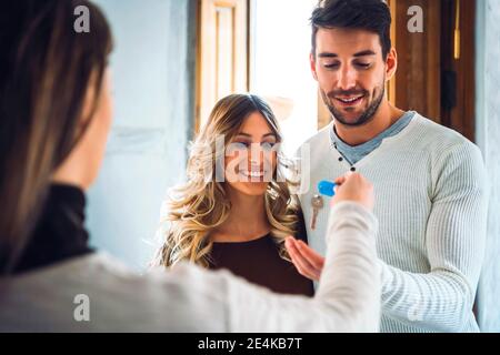 Estate agent handing over keys to happy young couple Stock Photo