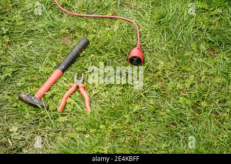 Extension cord, hammer and pliers lying on green grass Stock Photo