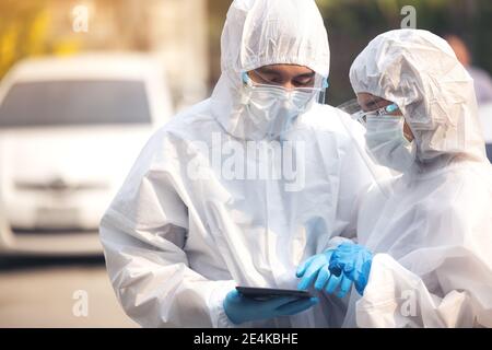 Doctors in ppe suit using tablet with face shield discussing standing on street Stock Photo