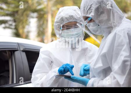 Doctors in ppe suit using tablet with face shield discussing standing on street Stock Photo