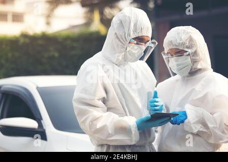 Doctors in ppe suit using tablet with face shield discussing standing on street Stock Photo