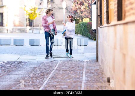 Young man and boy with ice cream and skateboard smiling while walking on footpath Stock Photo