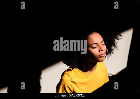 Young woman with eyes closed standing against wall Stock Photo