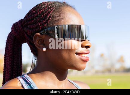 Happy sportswoman in sunglasses looking away against clear sky on sunny day Stock Photo