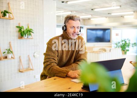 Businessman with headset talking while using digital tablet at office Stock Photo