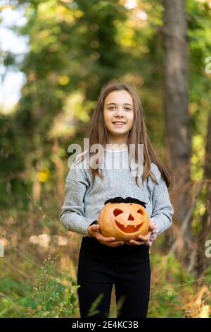 Smiling girl holding Halloween pumpkin while standing at park Stock Photo