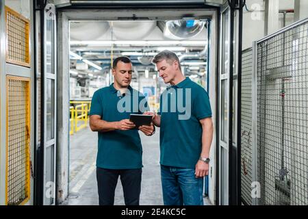 Male engineers discussing over digital tablet in factory Stock Photo