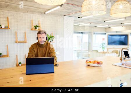 Mature businessman wearing headset using digital tablet while sitting at office Stock Photo