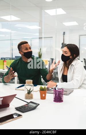 Male professional discussing plans with female coworker against glass during COVID-19 Stock Photo