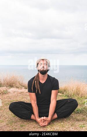 Young man practicing yoga while sitting on field against cloudy sky, Santander, Spain Stock Photo