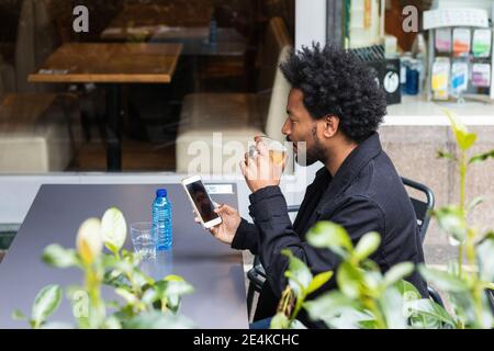 Man with afro hair having drink while using mobile phone at sidewalk cafe Stock Photo