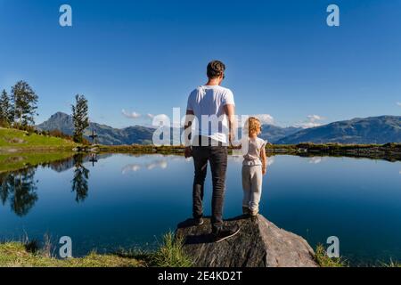 Father standing with little daughter on top of lakeshore boulder Stock Photo